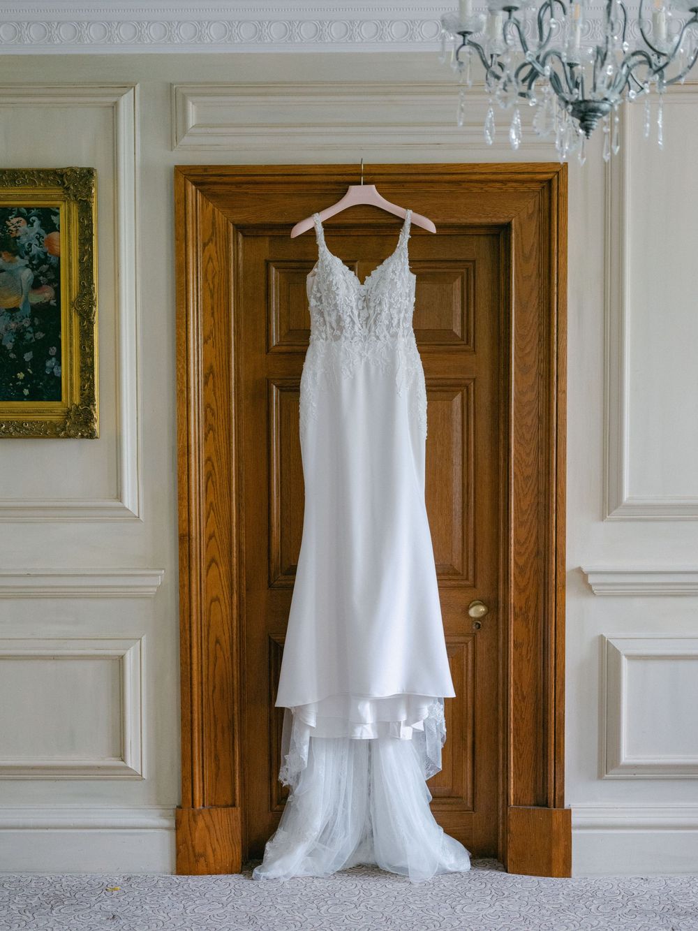 Elegant white lace wedding dress with train hanging on wooden door frame in bridal suite.