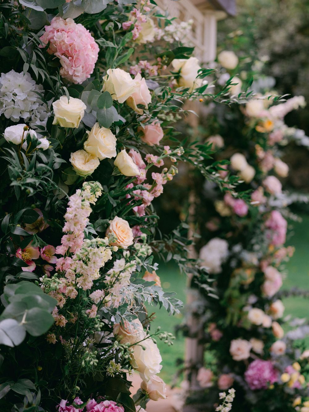 Lush floral arch with pink peonies, cream roses, and greenery for an outdoor wedding ceremony.