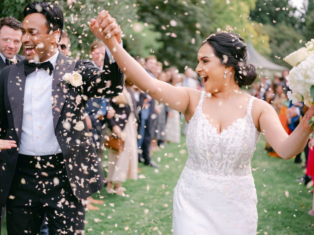 Bride and groom joyfully walking through confetti shower after outdoor wedding ceremony.