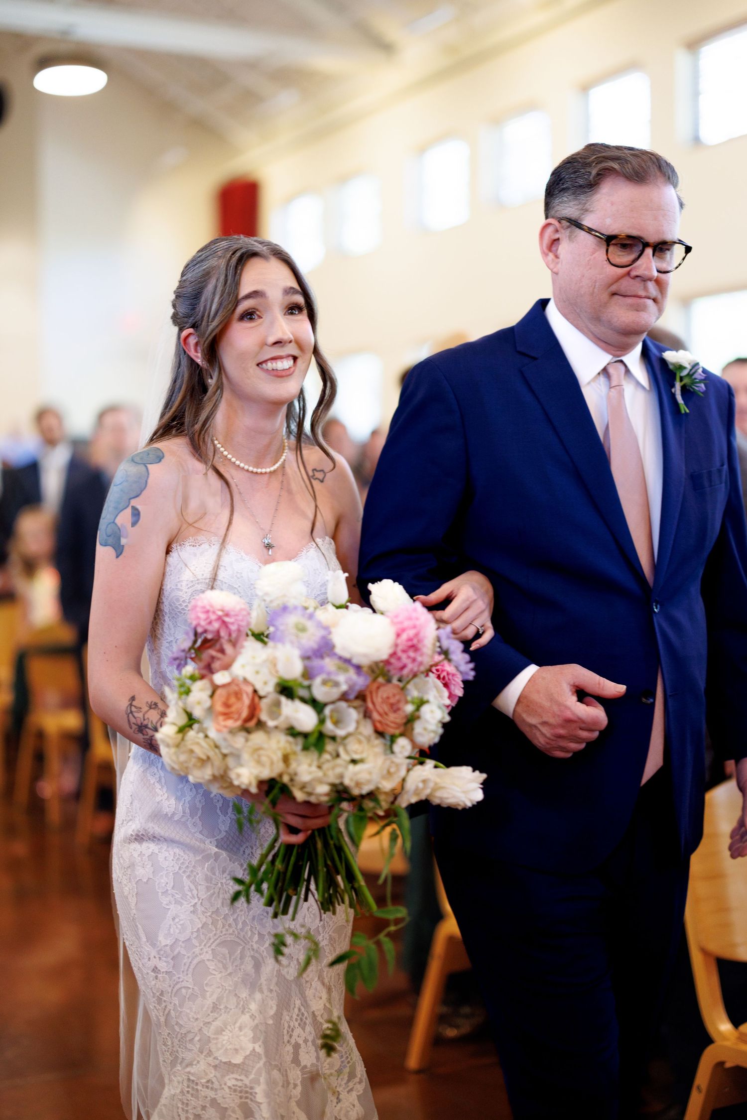 A joyful wedding ceremony processional with a bride in white lace gown carrying pink and cream floral bouquet.