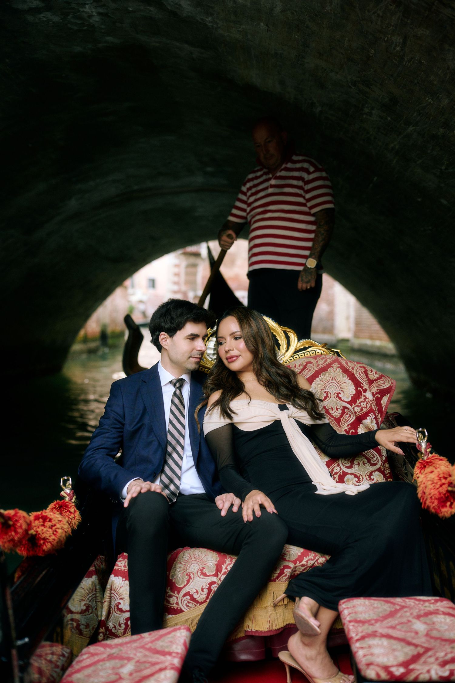 Couple sits on red and white patterned cushions under a stone archway during romantic photoshoot.
