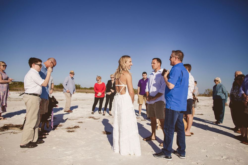 A series of people walking and gathering on a sandy beach during a sunny day with blue skies overhead.