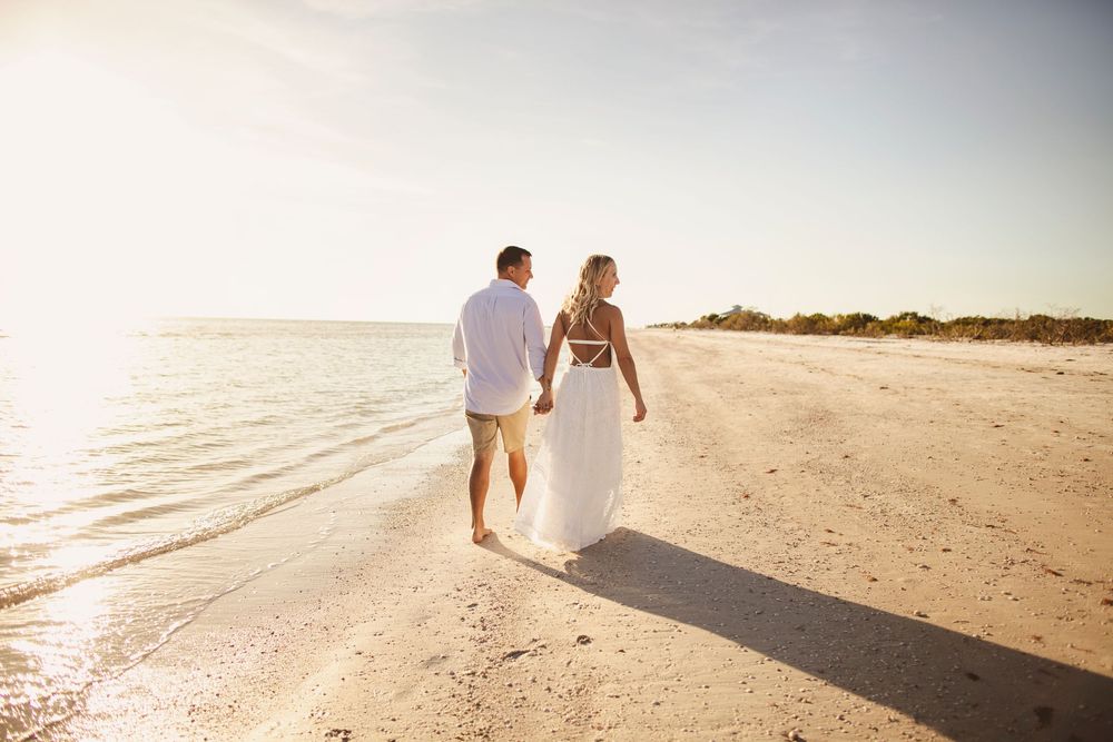 A couple walking together on a sandy beach at sunset casting long shadows behind them.