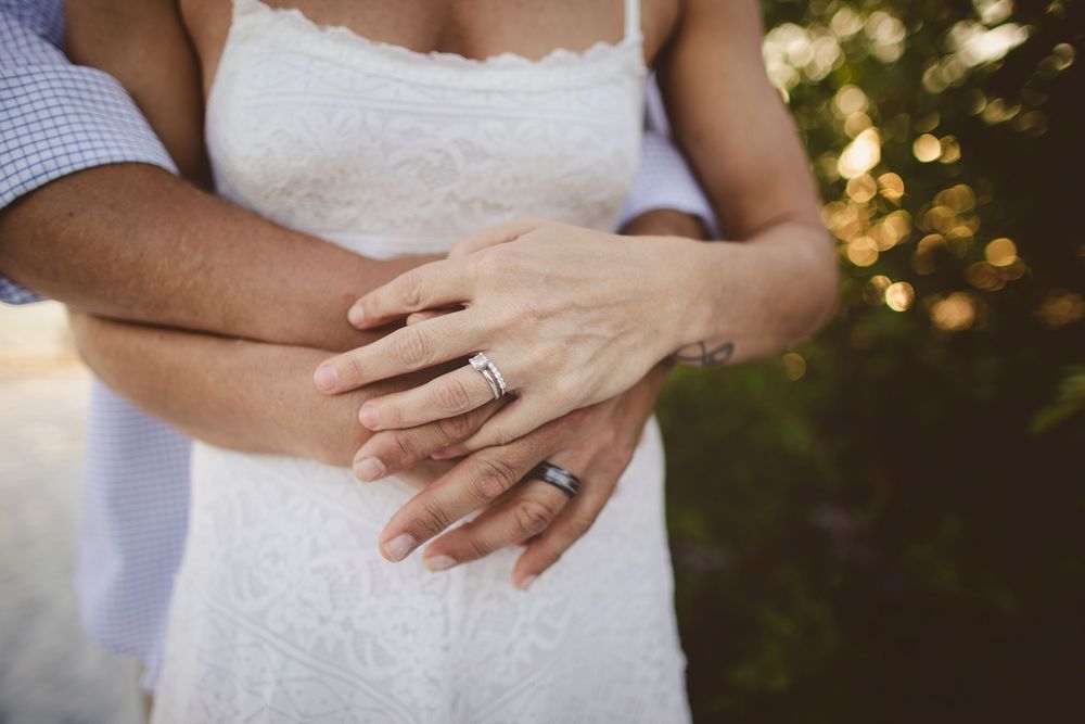 Close-up detail shots of a white lace wedding dress with hands gently touching the fabric in natural outdoor lighting.