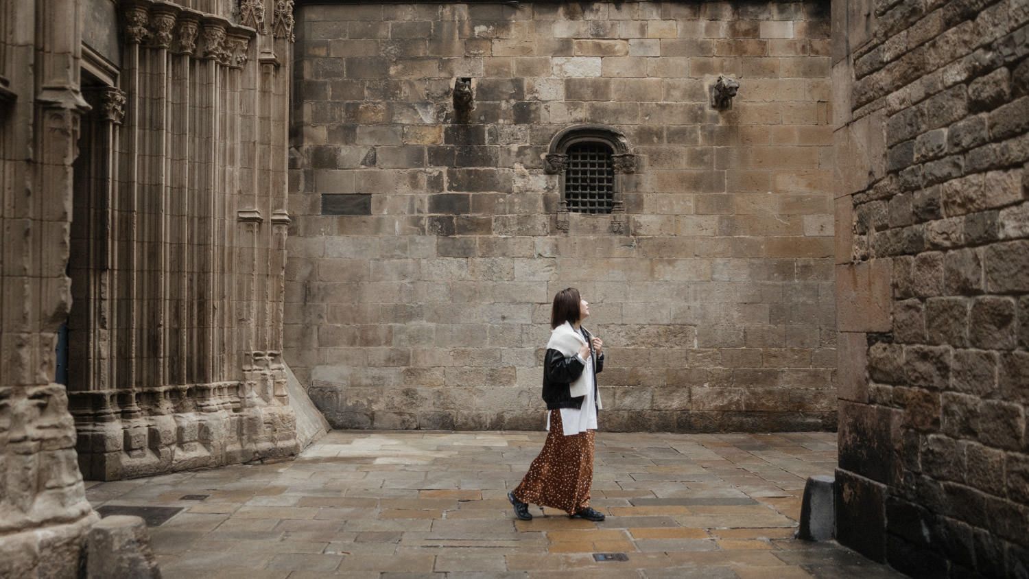 Person walking past ancient stone cathedral walls in a historic cobblestone courtyard.