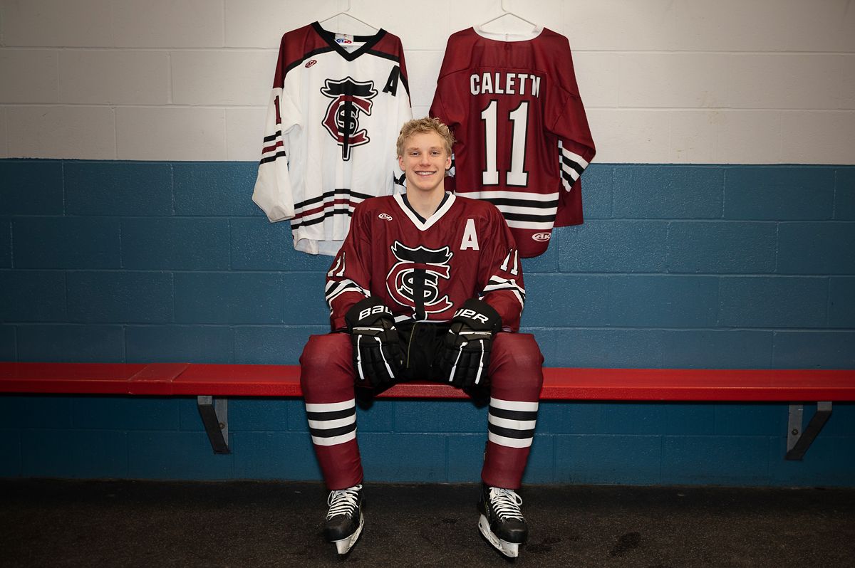 teen boy in full hockey gear sits on bench in change room with two jerseys on the wall behind him at Baltimore Community Centre*