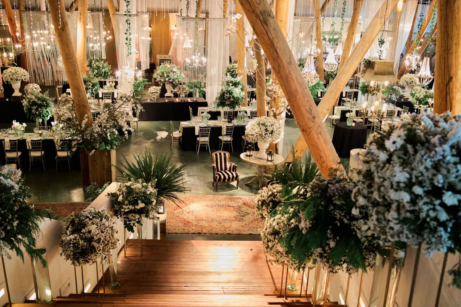 Rustic indoor wedding venue decorated with elegant white drapery, wooden beams, and lush floral arrangements.