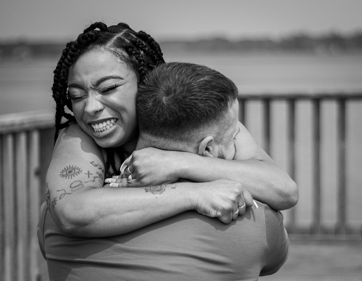 A joyful embrace captured in black and white photography on a waterfront deck.