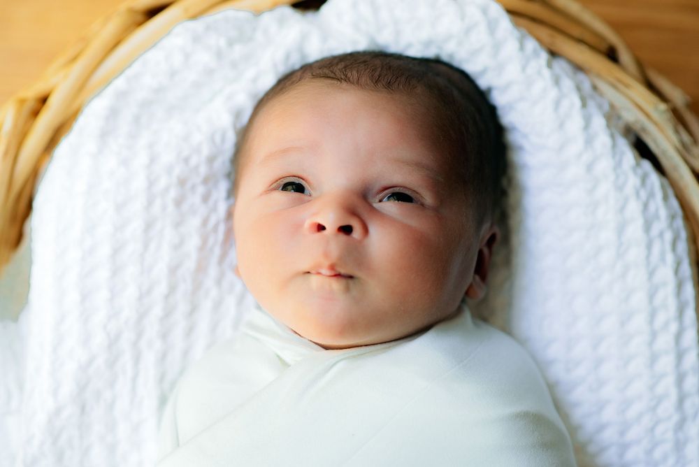 a newborn staring with open eyes and pursed lips wrapped up for his newborn in home session in Massachusetts
