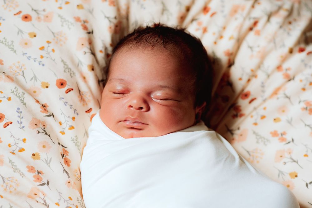 a newborn baby wrapped up and resting on a floral blanket.
