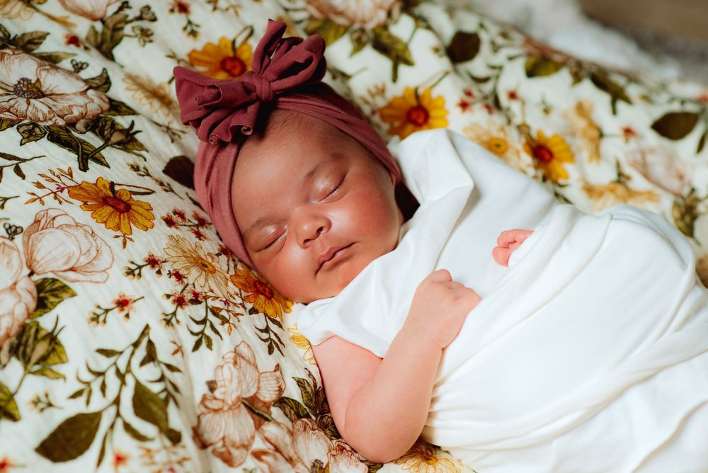 a newborn baby girl with hair bow sleeping peacefully in an in home newborn portrait session