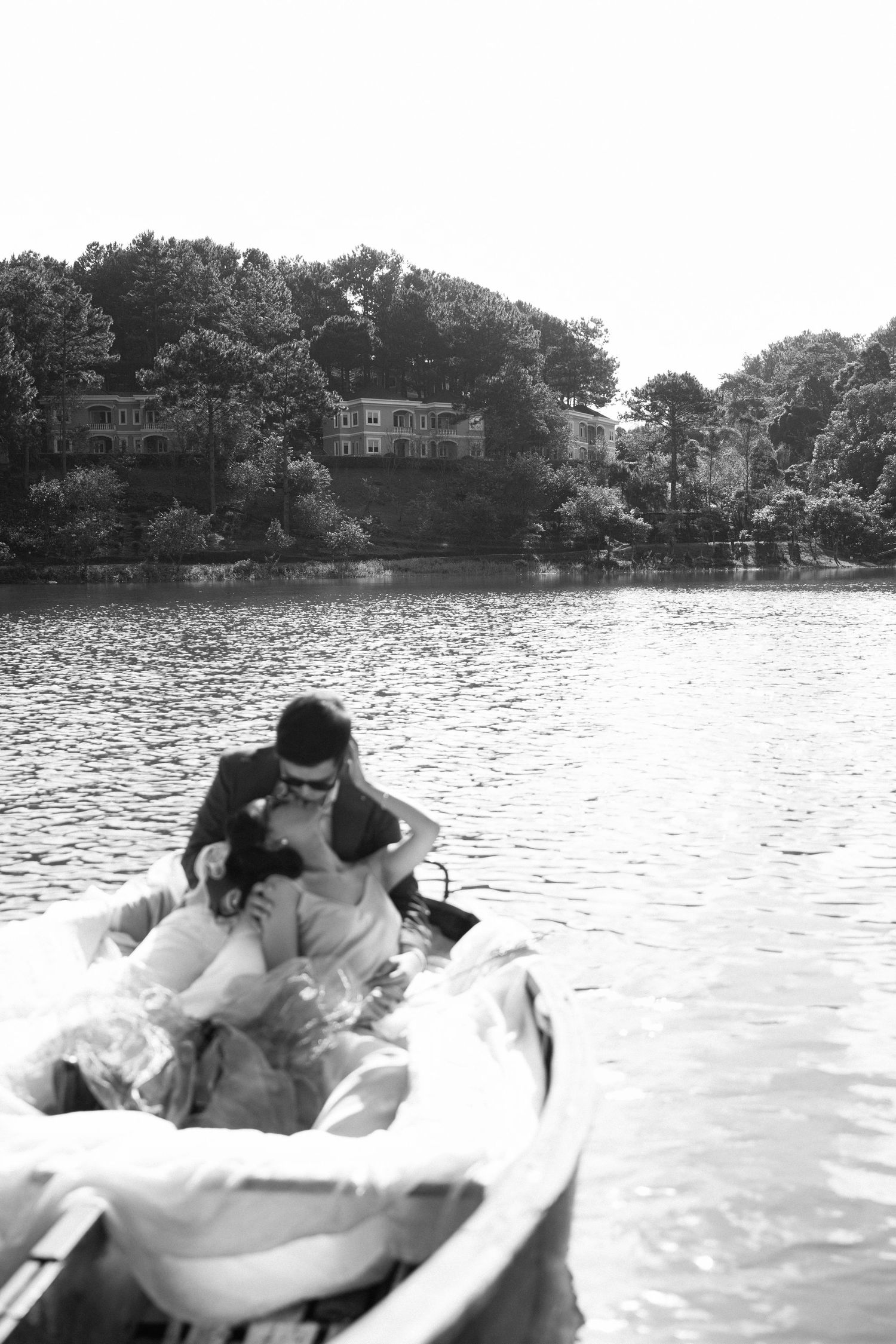 Black and white romantic wedding photo of couple embracing in a rowboat on a serene lake.