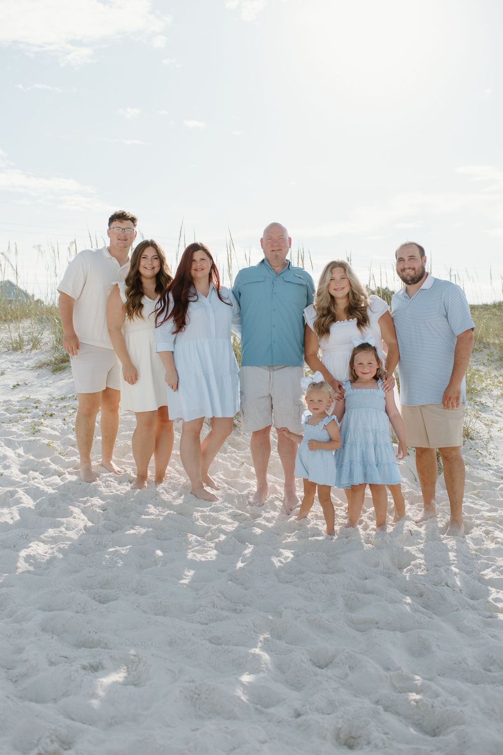 Extended family group poses together on a white sandy beach wearing coordinated casual outfits.