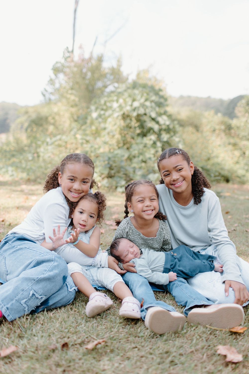 Children in casual denim and white outfits pose together on grassy ground.