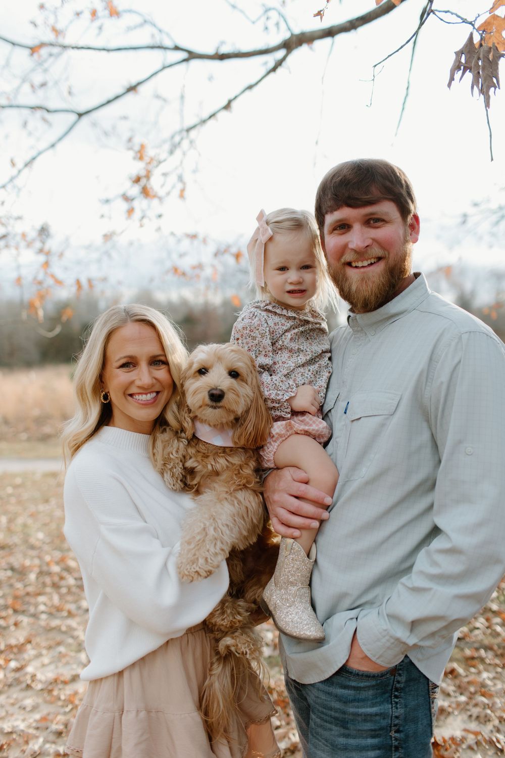 Family poses outdoors with their fluffy goldendoodle dog during autumn.