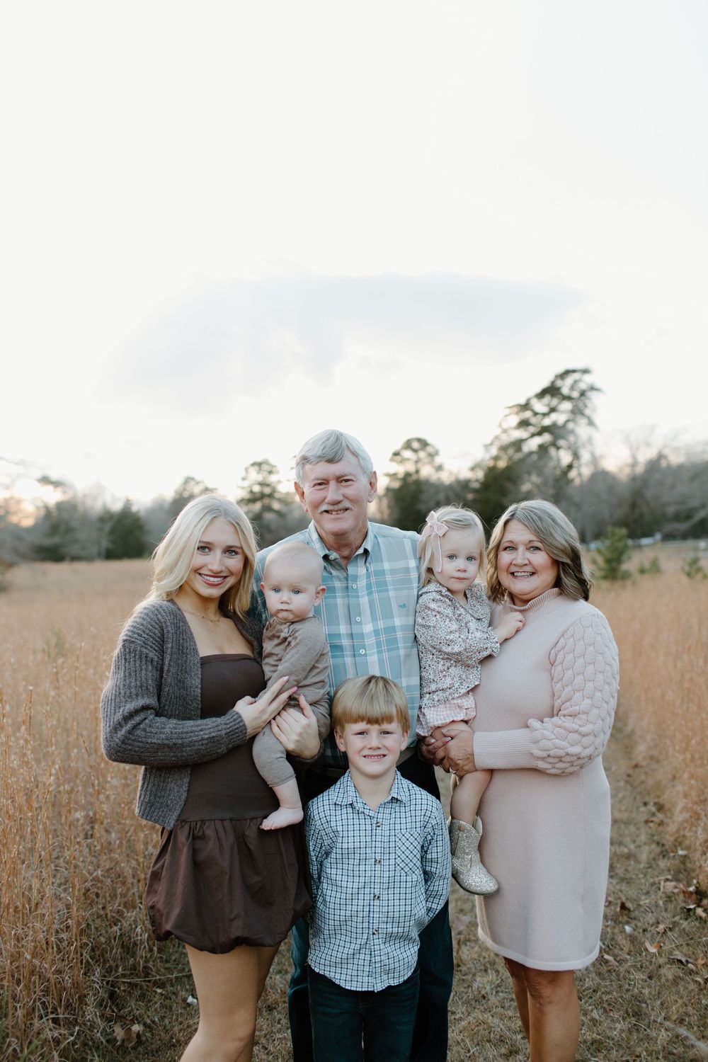 Multi-generational family gathering outdoors in field during golden hour.