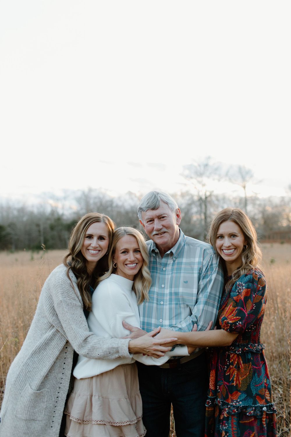 Extended family embraces while posing together in autumn field setting.