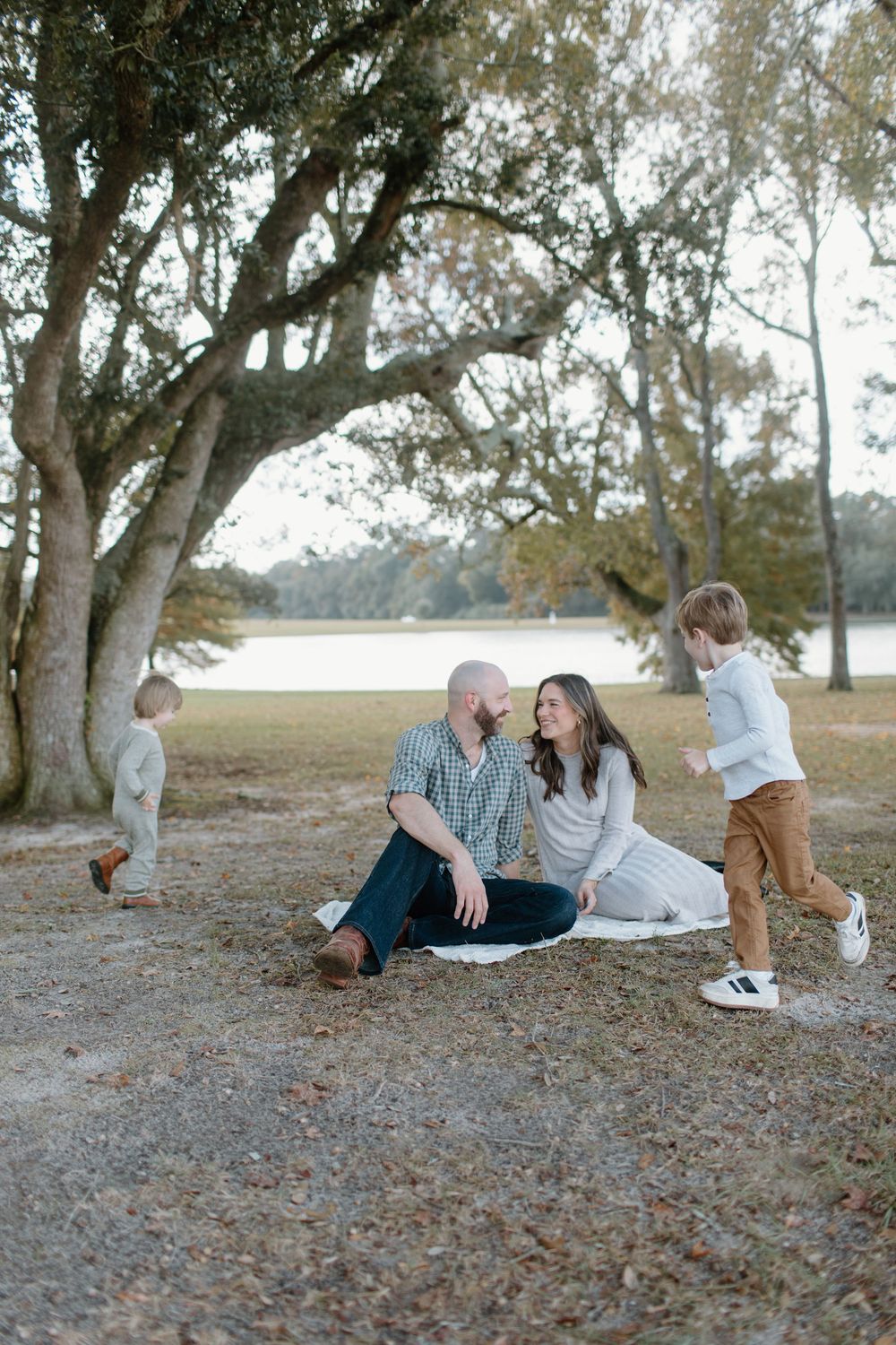 Group poses playfully lying on ground under trees covered in fallen leaves.