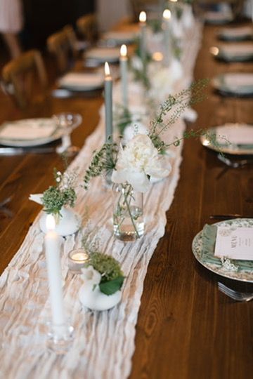 Elegant wedding reception table with white floral centerpieces, taper candles, and a lace runner on a rustic wood table.