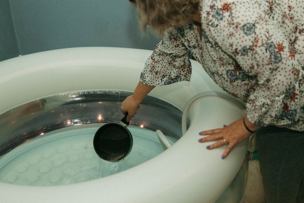 Midwife pouring warm water into inflatable birth pool preparing for home water birth.