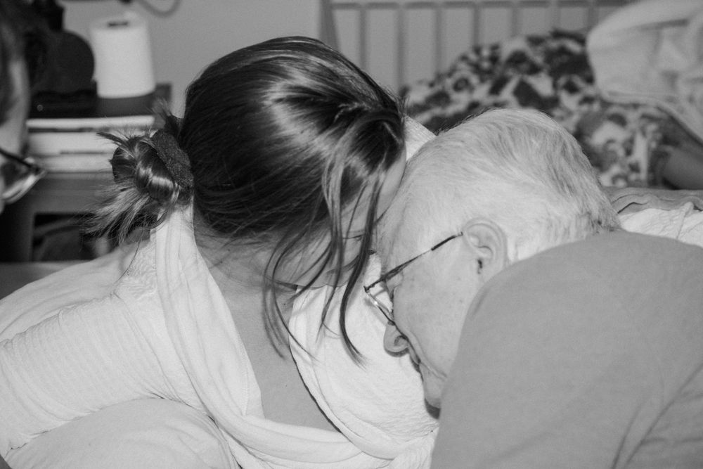 Black and white image of woman tenderly resting her head against laboring partner during home birth.
