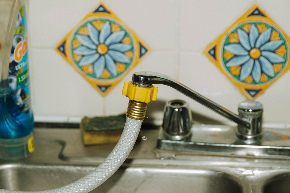 A flexible hose connected to a kitchen faucet with decorative blue floral tiles in the background.