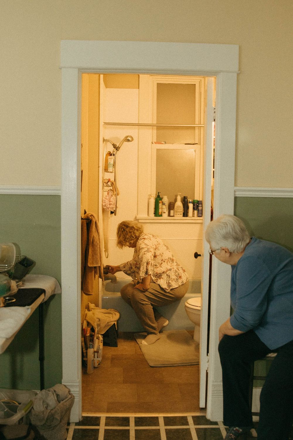 Midwife crouching in bathroom doorway assisting laboring woman while support person waits nearby.