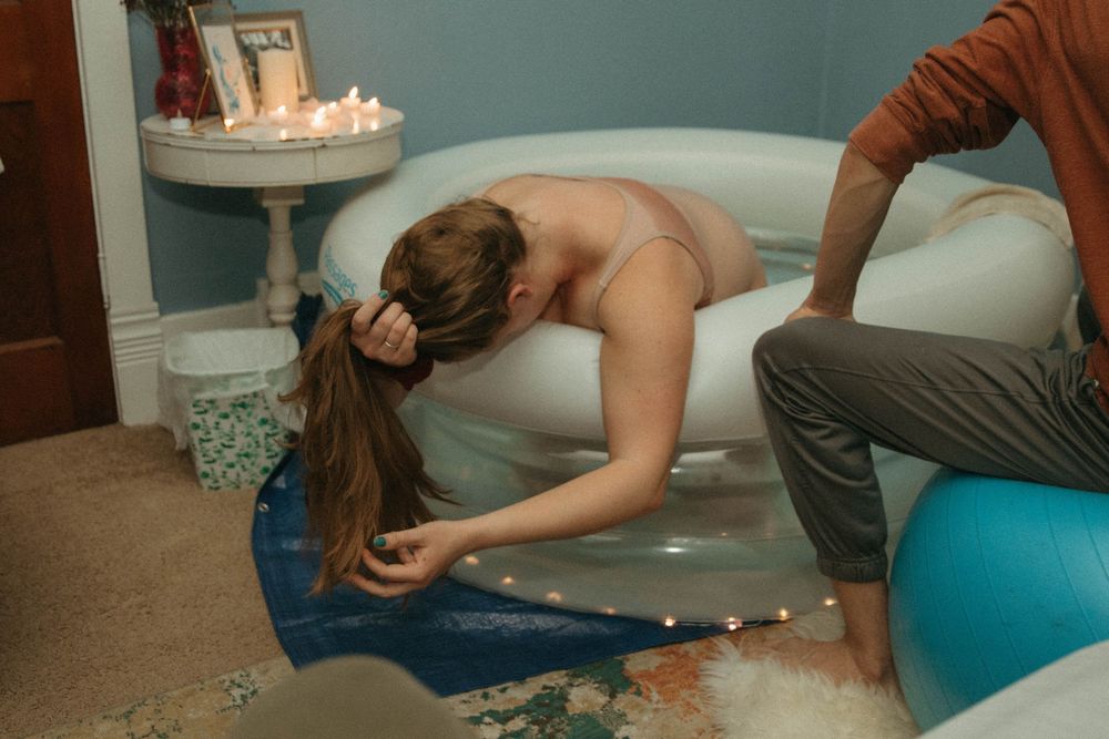 A woman laboring in an inflatable birth pool at home with a support person beside her.
