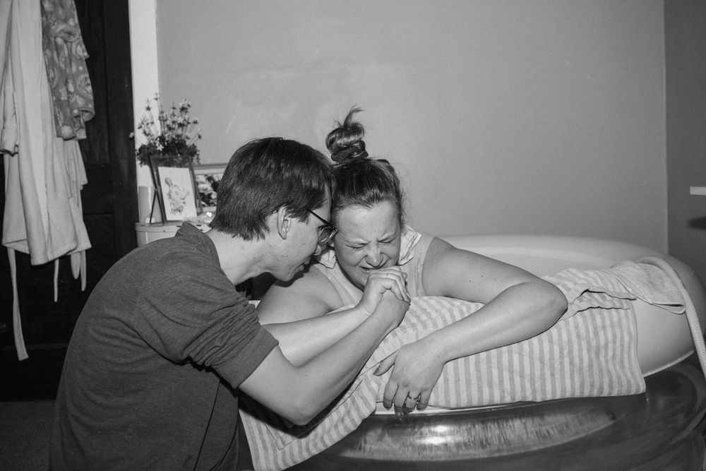 Black and white image of a couple during home water birth labor in an inflatable tub.