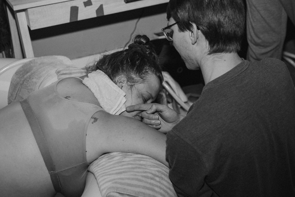 Black and white photo of a woman in active labor supported by her partner at home.