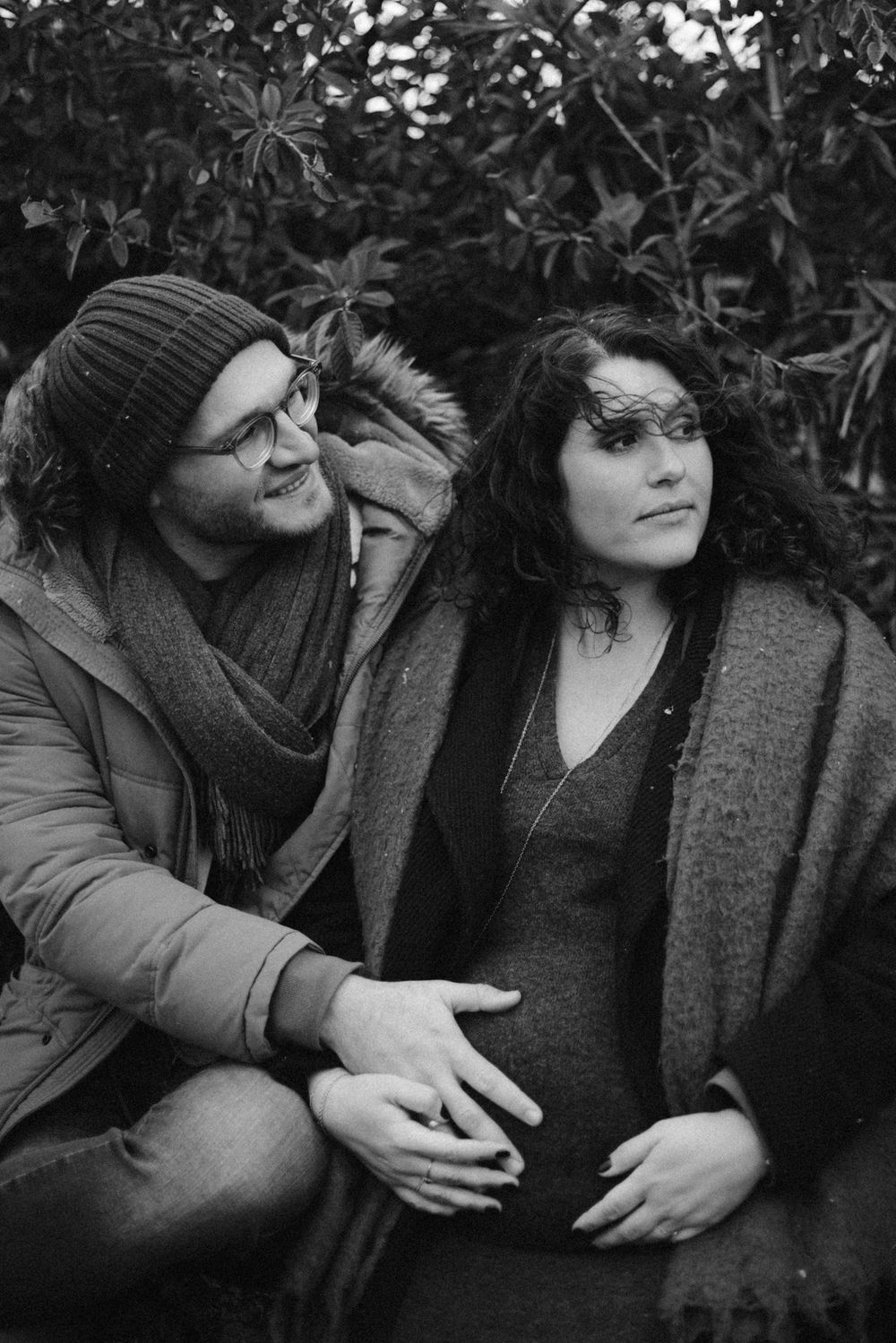 Black and white portrait of a couple sitting together outdoors with foliage in the background.