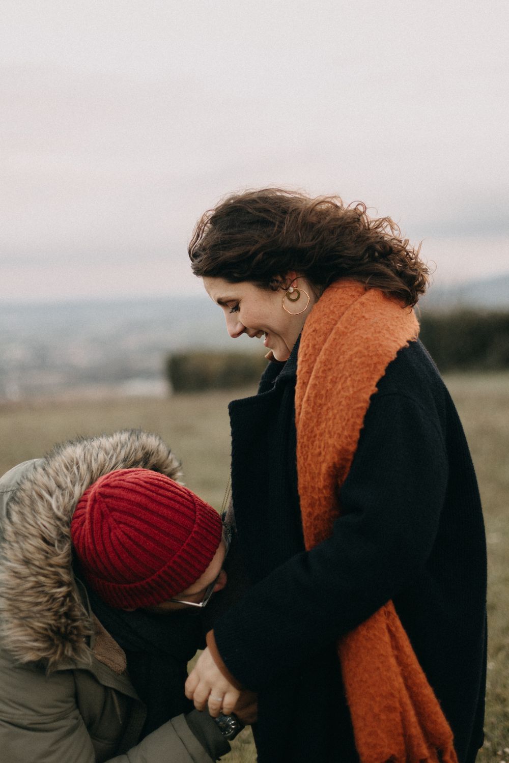 Two people in winter clothing share an intimate moment outdoors against a cloudy landscape.