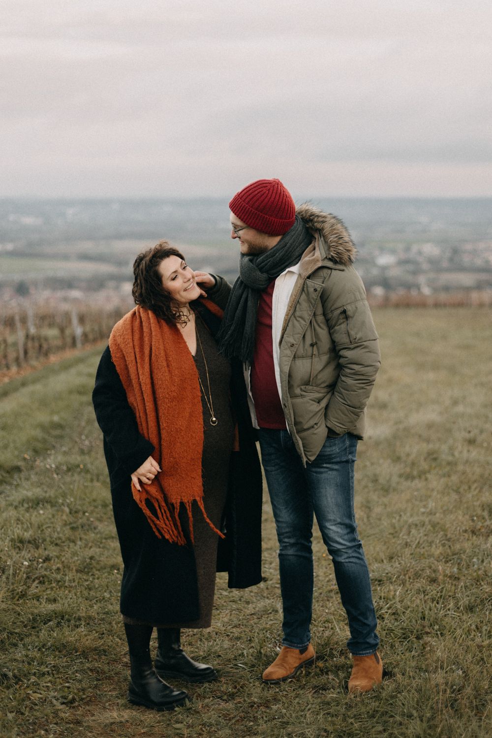 Couple shares tender moments together while standing in a grassy hilltop field with scenic countryside views.