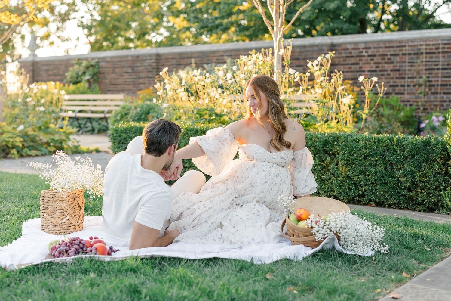 An expecting couple on picnic blanket surrounded by glowing sunlight, fruit, and delicate floral during a maternity session in Pittsburgh.