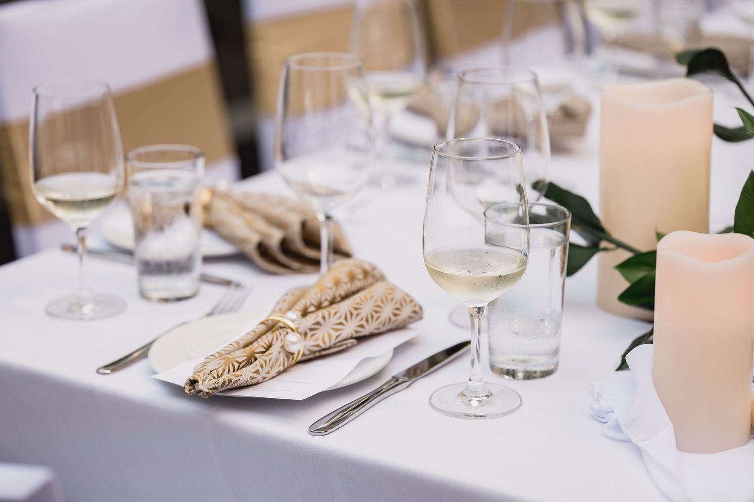 Elegant table setting with white linens, wine glasses, and wheat stalks on plates in a minimalist style.
