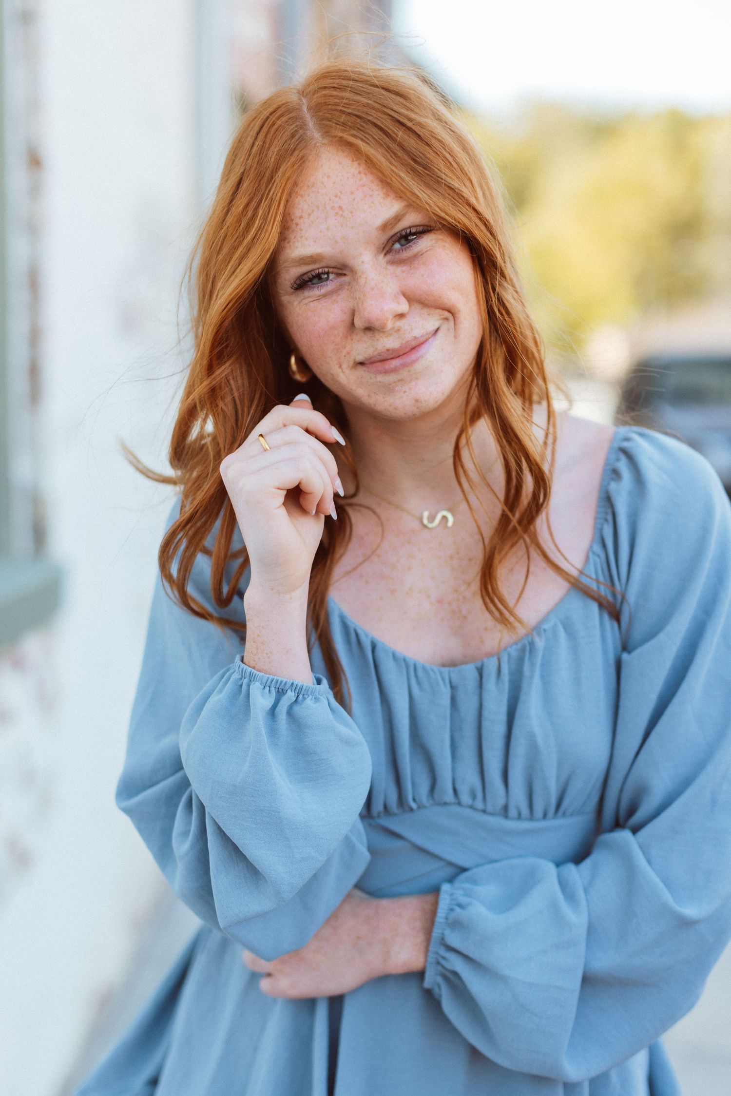 A red-headed young woman in a blue dress smiles for the camera during her senior photo session near Kansas City, Missouri.