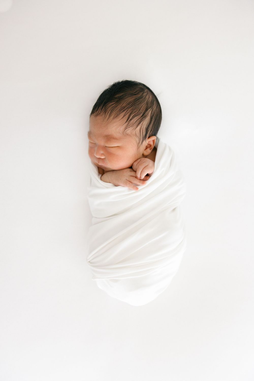 Minimalist portrait of sleeping newborn swaddled in white fabric on light background in the Connecticut Studio.