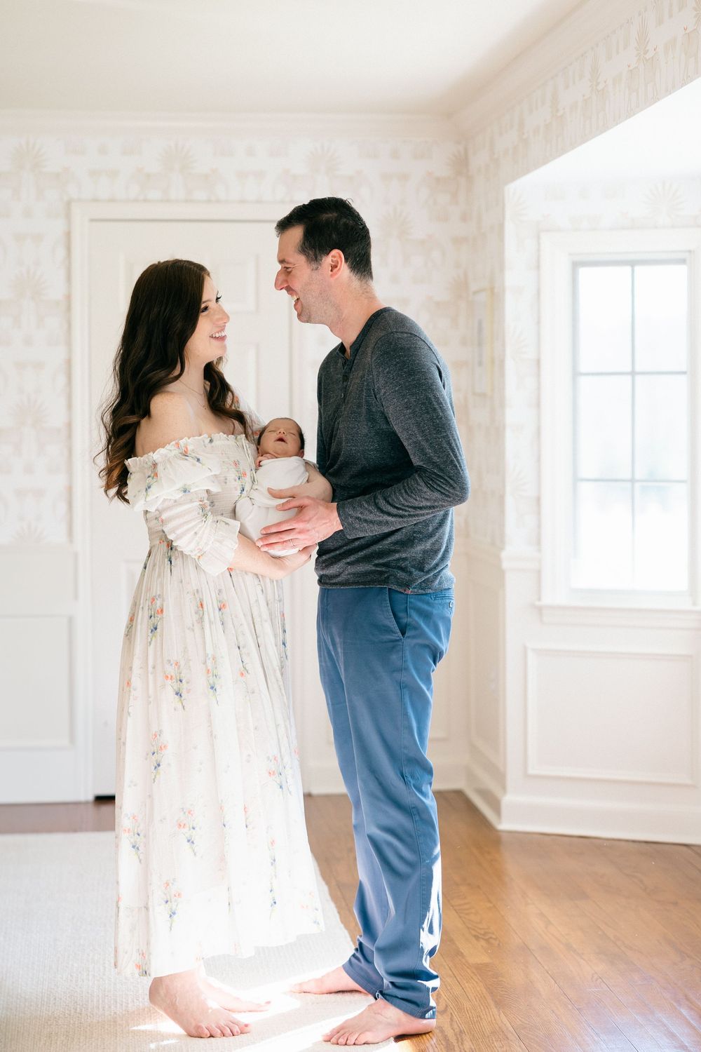 Family sharing tender moments with newborn in bright sunlit room with hardwood floors in their in-home session.