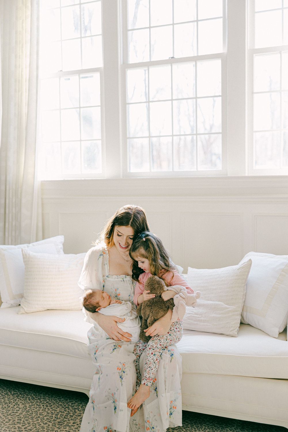 Intimate family moments on white couch in bright, airy room with large windows in Greenwich Connecticut home.