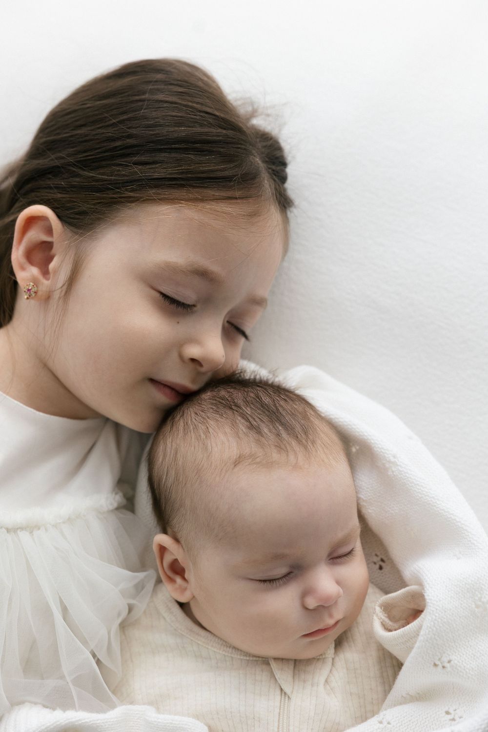 Tender moment of gentle embrace between parent and sleeping infant in soft white setting in the Connecticut Studio.