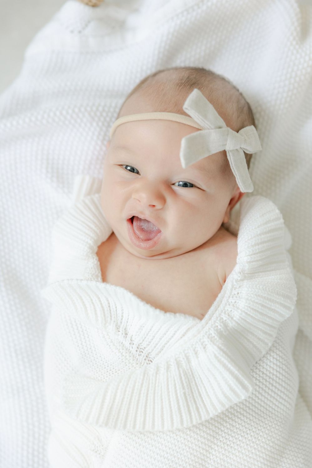 Newborn baby wearing white bow and ruffled collar smiles during professional photo session in the Essex, Connecticut Studio.