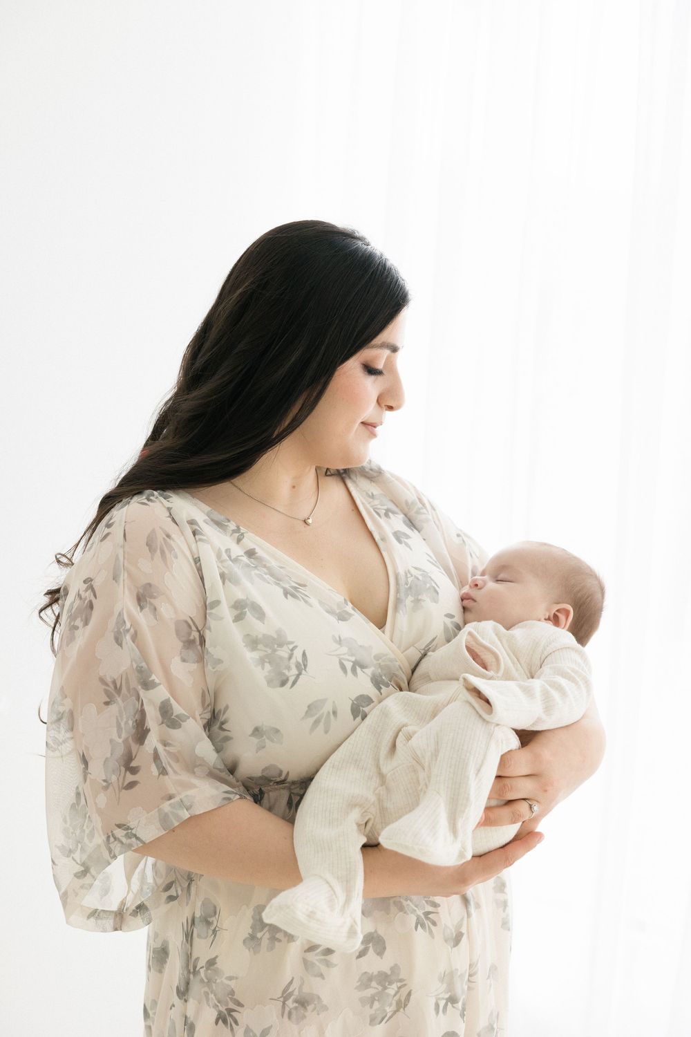 Mother in floral dress holds newborn baby during elegant studio portrait session in the Connecticut Studio.