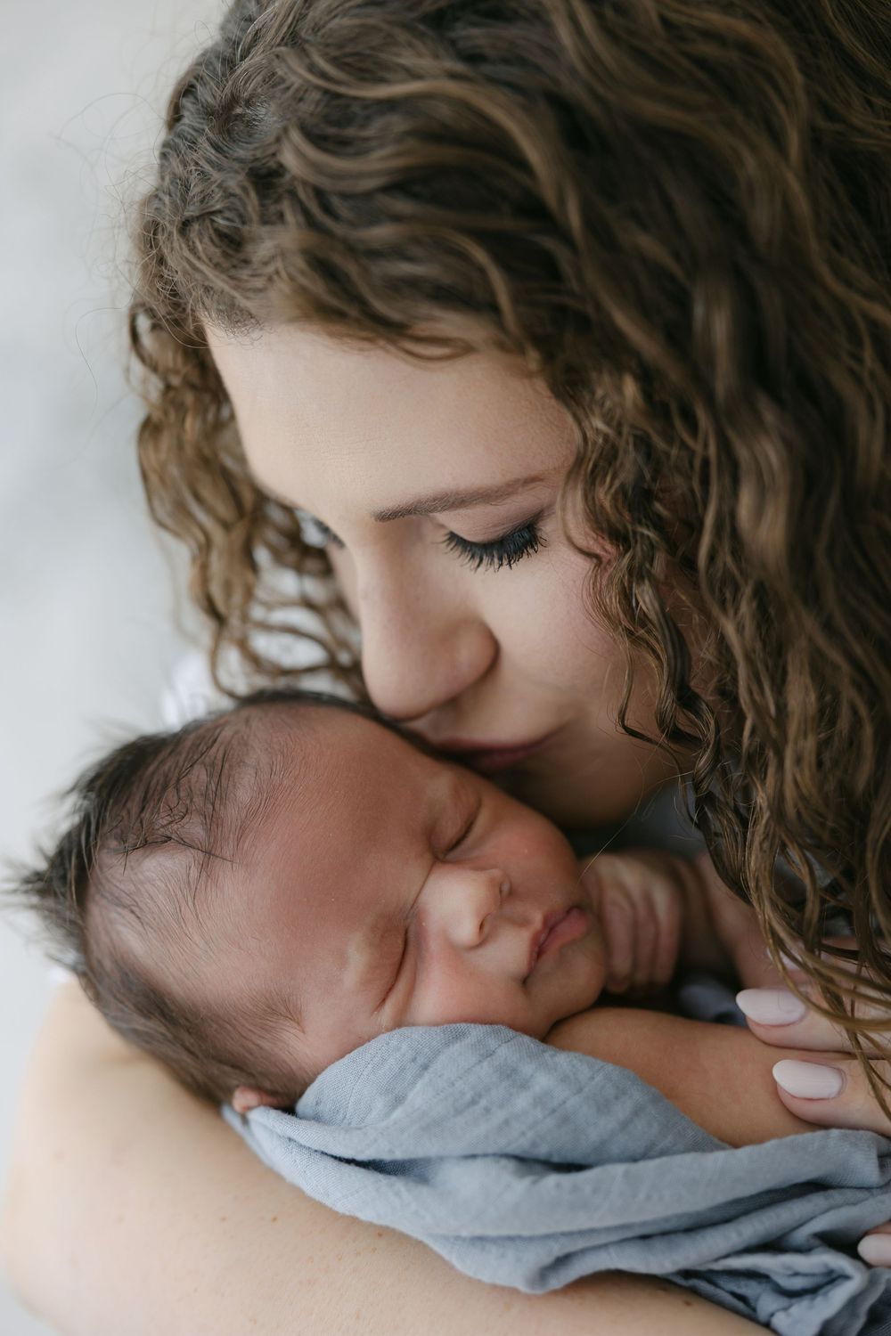 Intimate newborn photography session showing gentle moments with baby in grey wrap in the Connecticut Studio.