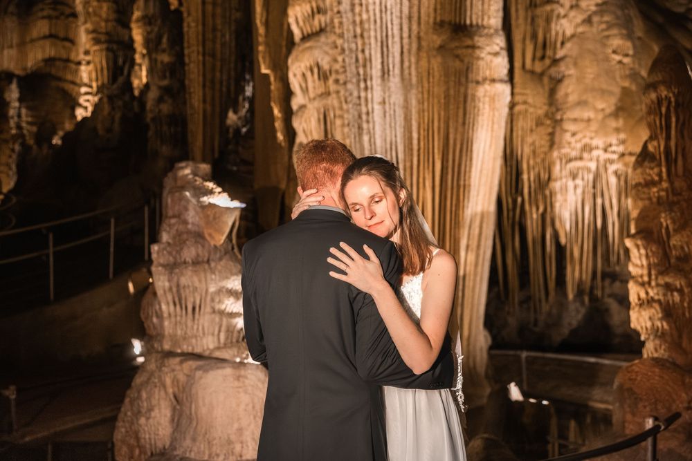 Couple embracing in a romantic moment inside a beautifully lit limestone cave with dramatic stalactites and stalagmites.