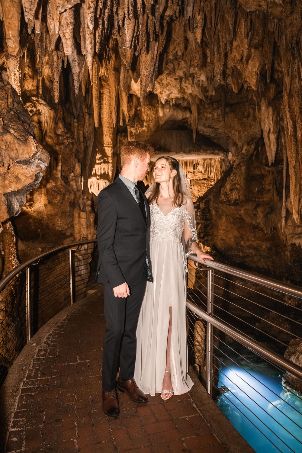 A romantic moment captured in a dimly lit cave with stalactites and stalagmites, illuminated by soft lighting.