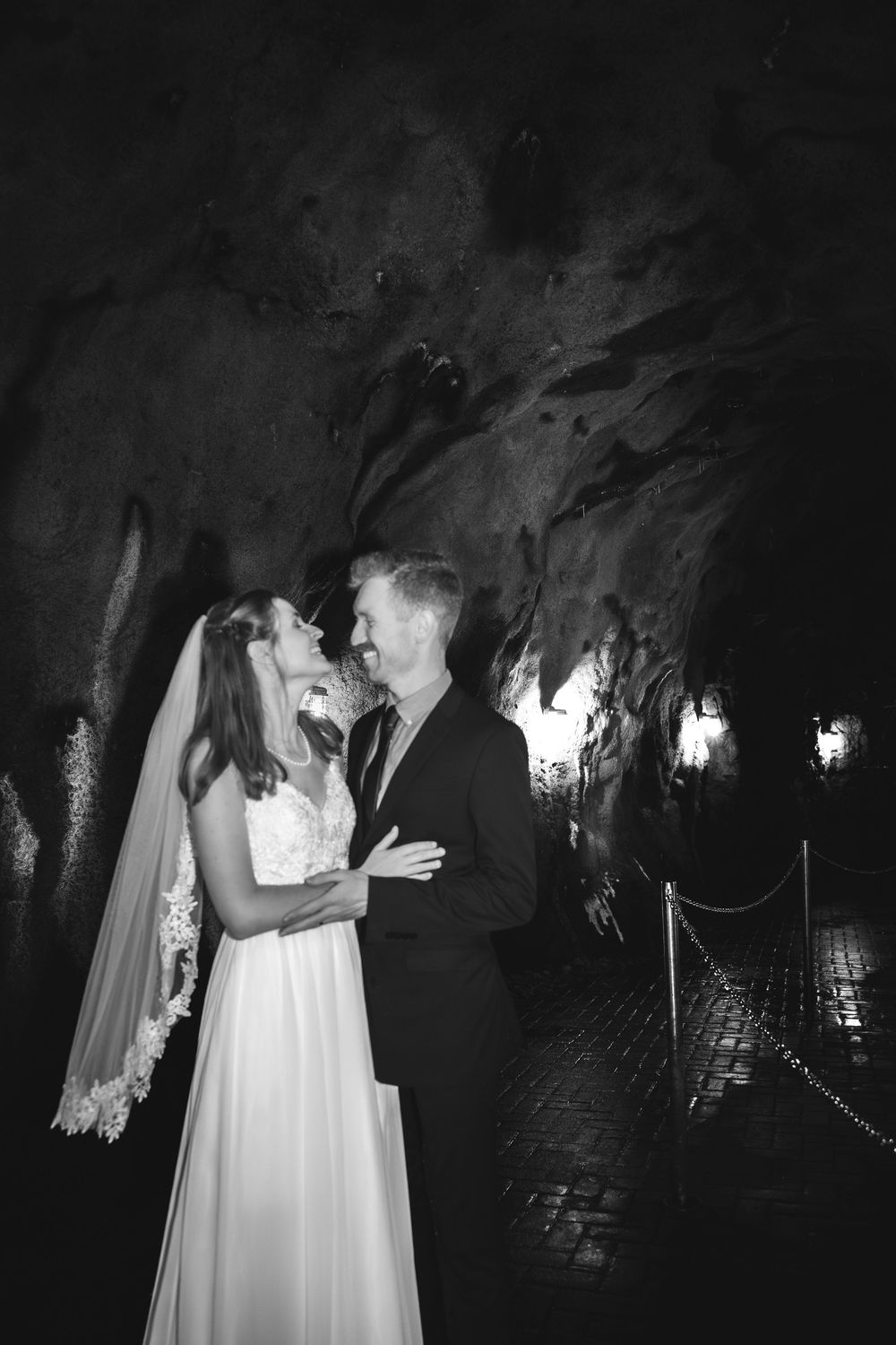 A romantic black and white wedding photo sequence showing a couple embracing in a dimly lit cave or tunnel setting.