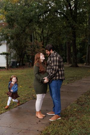 A couple stands together on an autumn path while a small child runs playfully in the background.