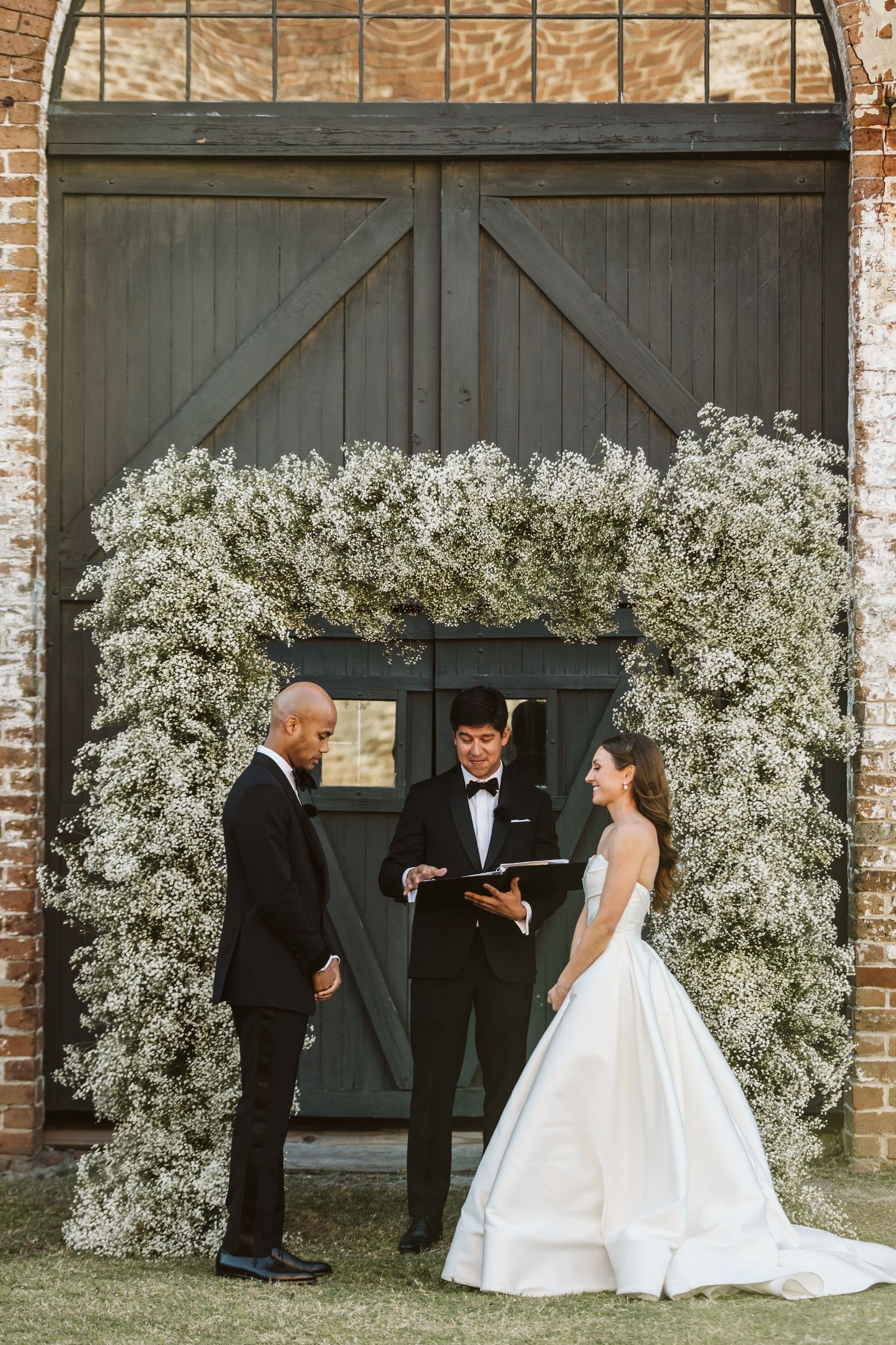 A wedding ceremony setup with a baby's breath floral arch against rustic wooden barn doors.