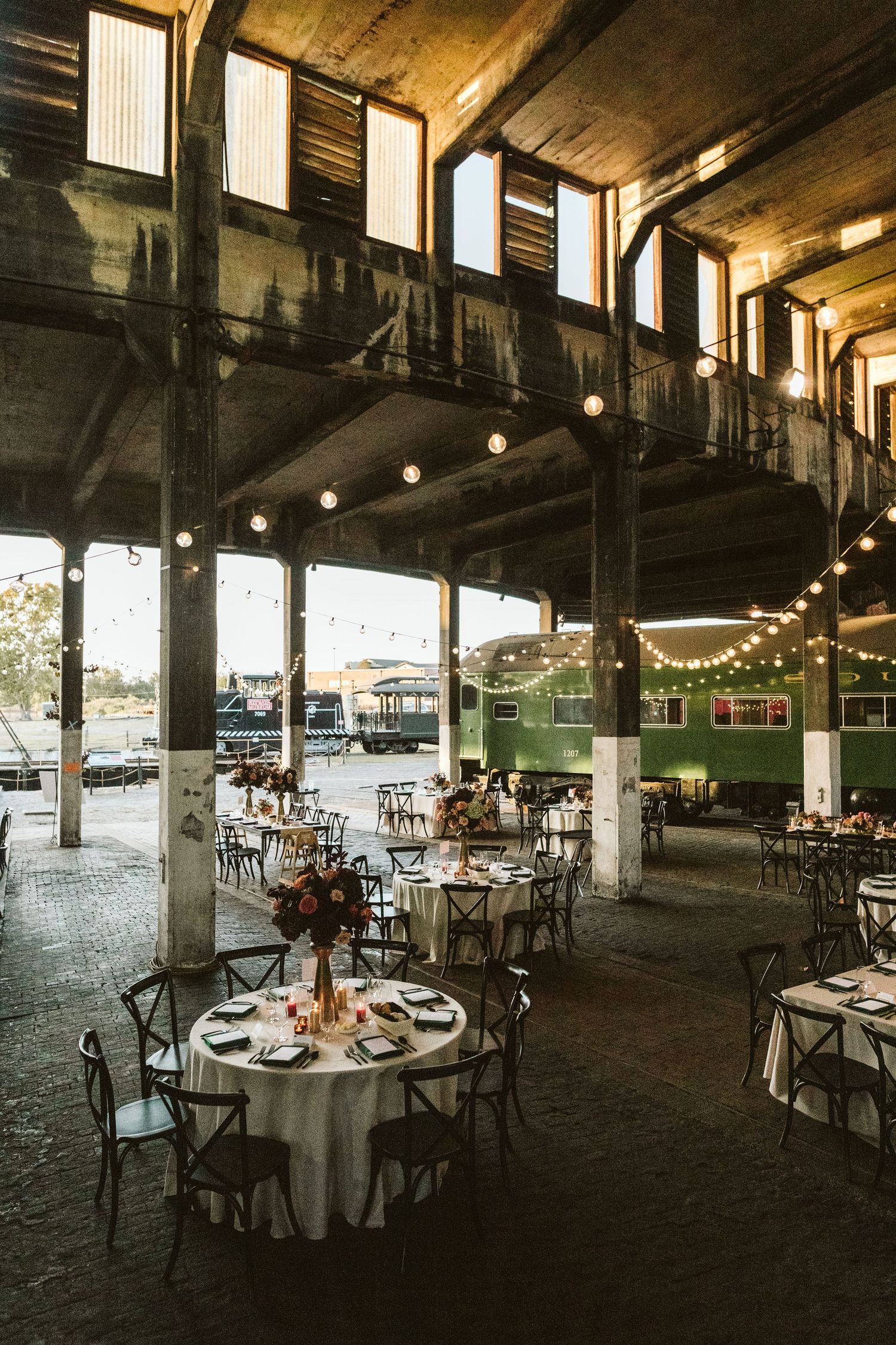 Elegant wedding reception venue with round tables set under rustic wooden beams and warm lighting.
