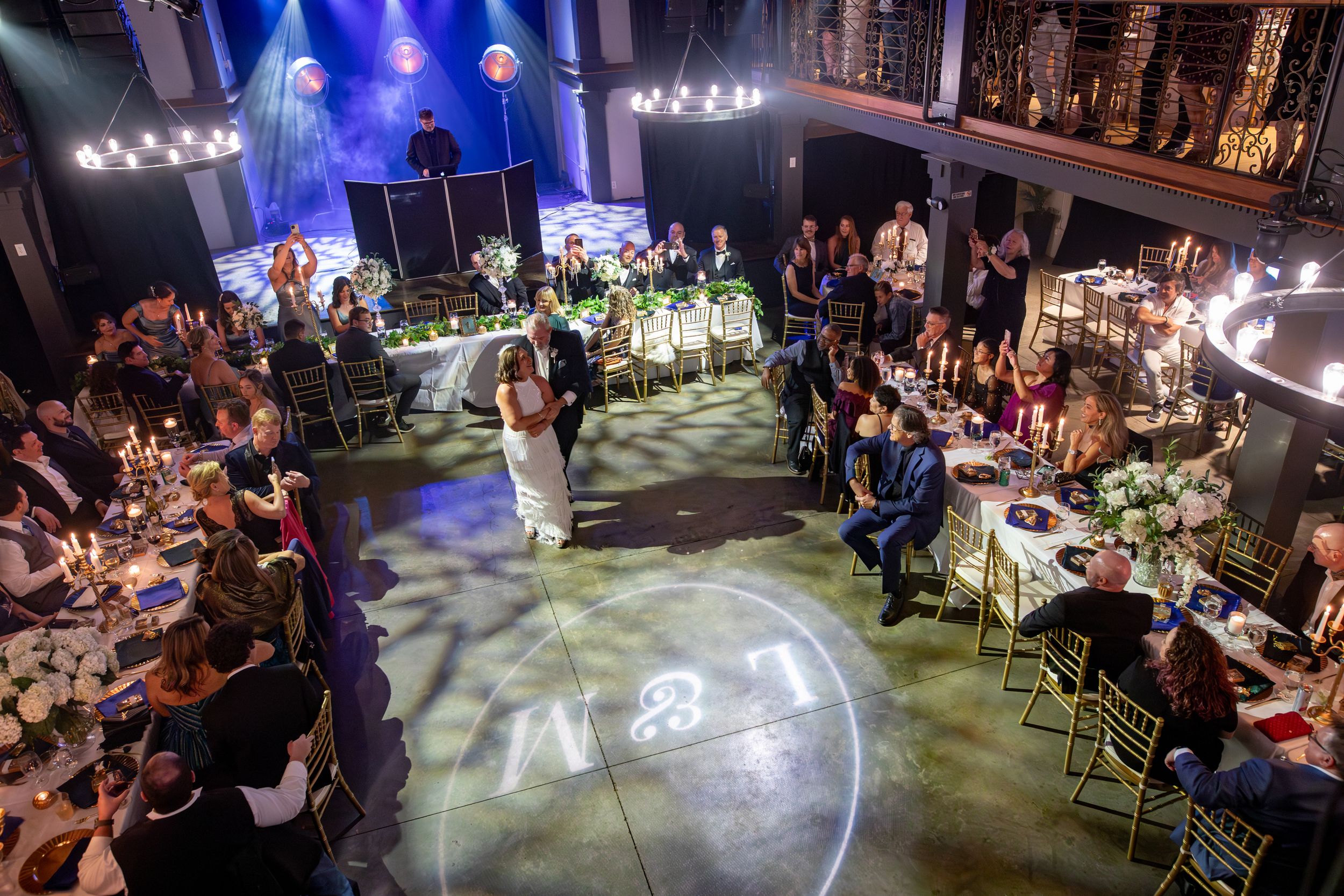 Dimly lit banquet hall with guests seated at decorated tables under atmospheric blue lighting and chandeliers.
